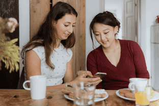 an image of two women lying on a bed looking at a phone